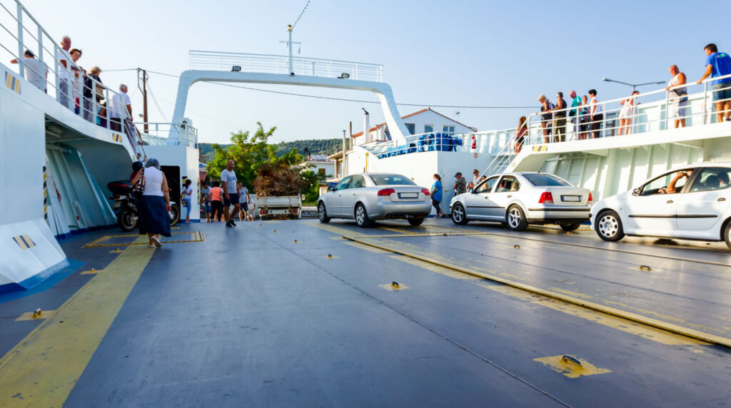Conducteur préparant sa voiture familiale pour l'embarquement ferry, vérifiant les documents près du véhicule avec coffre ouvert et bagages organisés